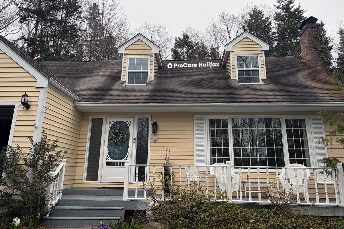 Ground-level view of a residential home in Beford, Nova Scotia, showing a roof stained with black algae streaks and moss growth prior to treatment.