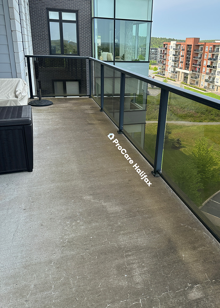 Weathered and stained concrete balcony floor with outdoor furniture and railing prior to professional cleaning